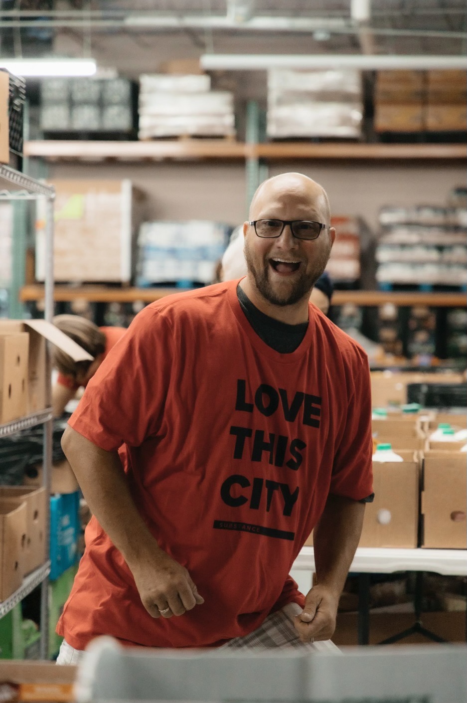 Man in warehouse smiling wearing t-shirt that says "Love This City"